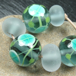 Both the rounds and spacers are made with a core of Slate under Effetre Clear. The spacers have been tumble etched and the rounds decorated with large Effetre white dots under Aegean and Elphaba.